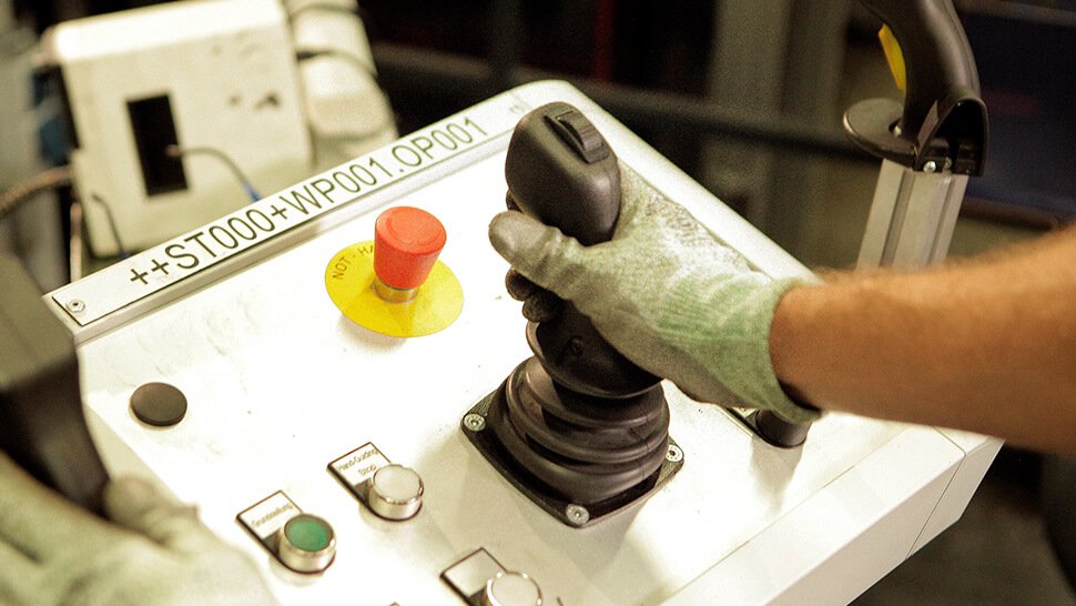 Der Mitarbeiter steuert den Kuka-Roboter mittels Joystick. Dadurch kann er eine angenehme Körperhaltung einnehmen, um die Bauteile auf Fehler zu prüfen.  