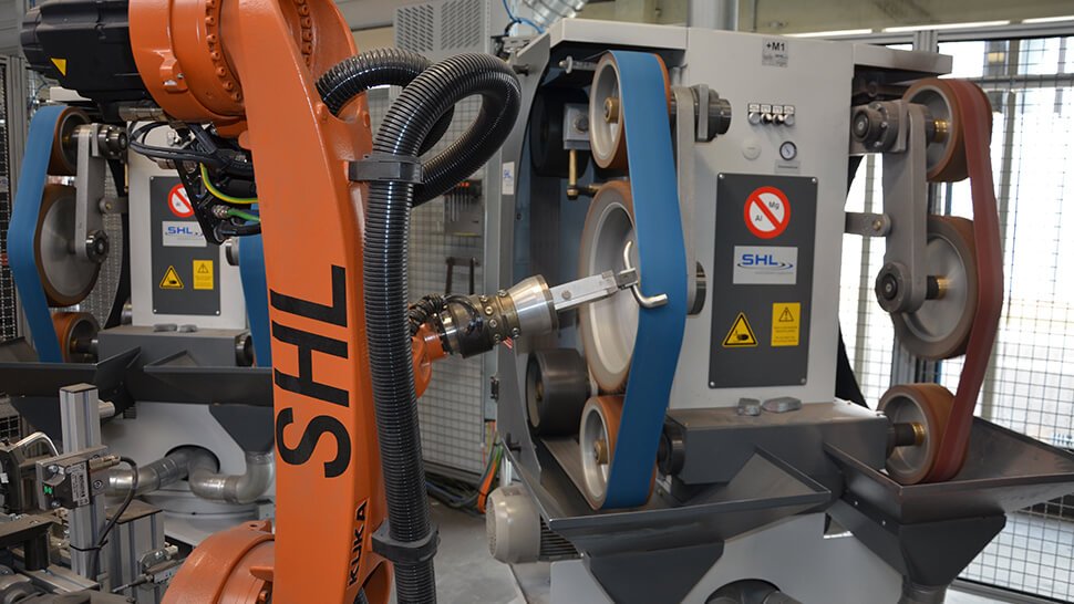 Der Roboter führt die Werkstücke zur Bearbeitung an die Doppelfreiband- und Kontaktrollenschleifmaschine DKS von SHL.