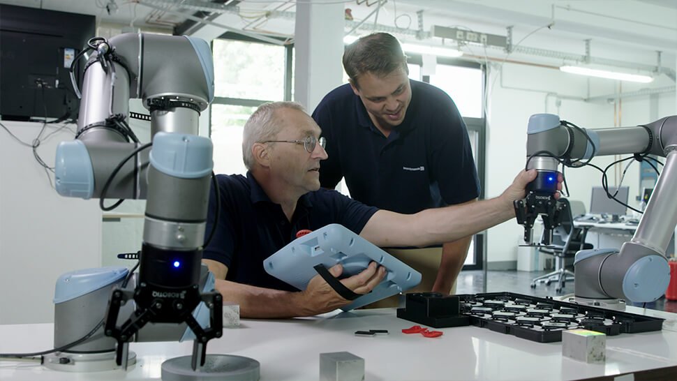 Peter Härtel und Jörg Lang programmieren die Roboter bei Beyerdynamic im sogenannten Teach Modus. Damit kann jeder Anwender den Roboterarm greifen und ihm neue Aufgaben beibringen, indem er ihn per Hand von Wegpunkt zu Wegpunkt führt.